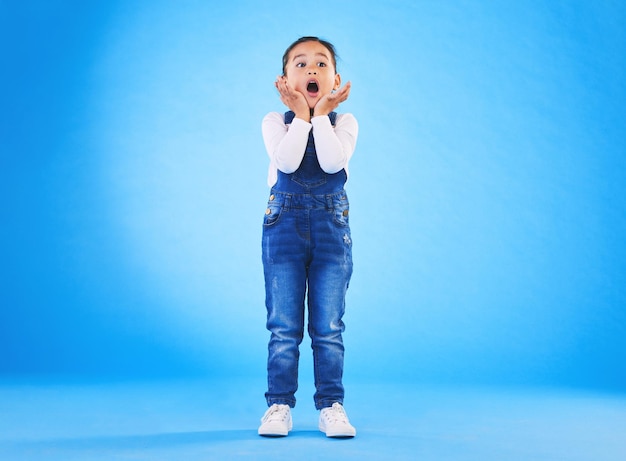 Geschokt wow en meisje verrassing met handen in de studio met angst en bang voor gevaar Alarm blauwe achtergrond en jong kind uit Hawaï met eng omg en emoji gezicht van een kind in gevaar