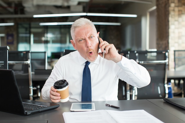 Geschokte emotionele zakenman die op telefoon spreekt