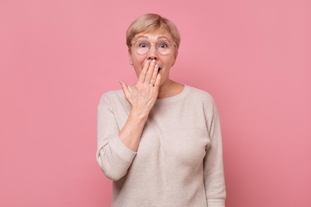 Geschokte en verbijsterde oudere vrouw die mond bedekt met handpalm van verbazing