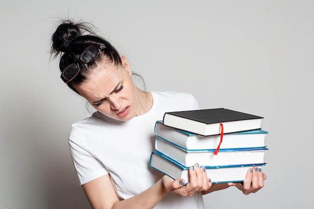 Geschokte jonge studente met een bril op het hoofd houdt een stapel boeken in haar handen