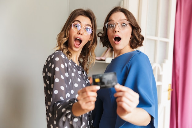 Geschokte jonge vrouwen shopaholics die creditcard tonen.