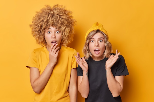 Geschokte jonge vrouwen staren met uitpuilende ogen reageren op vreselijke scène adem inhouden gekleed in casual t-shirt staan naast elkaar geïsoleerd over gele achtergrond Menselijke reacties concept