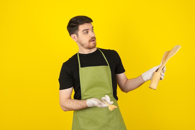 Geschokte kerel die houten lepels op geel bekijkt.