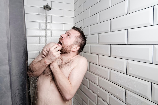 Geschokte man kijkt naar een gieter in de doucheruimte waaruit onverwacht koud water komt
