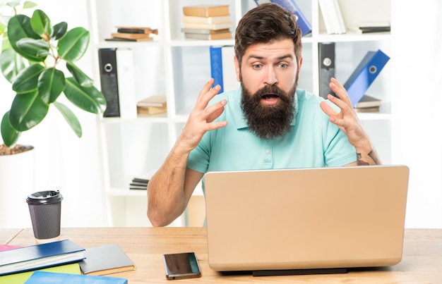 Geschokte man met open mond starend in laptop naar bureauschok