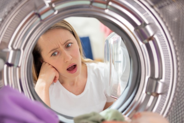 Geschokte vrouw kijkt in de trommel van de wasmachine opent de deur horror gekleurde kleding