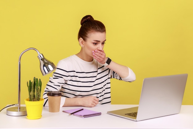 Geschokte vrouwelijke kantoormedewerker die haar mond bedekt en met een angstige uitdrukking naar het scherm van de laptop kijkt