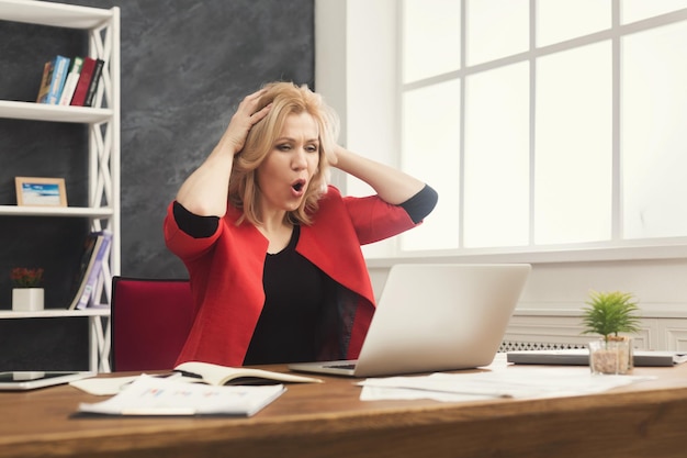 Geschokte zakenvrouw die op laptop werkt en problemen heeft, vrouw die op haar werkplek zit, kopieer ruimte