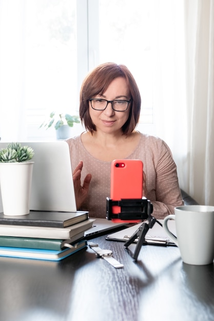 Geschoolde vrouw van middelbare leeftijd online communiceren of studeren op afstand via de telefoon op het statief,