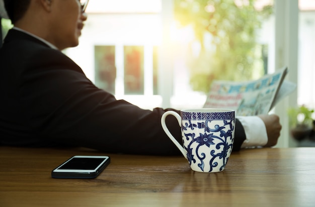 Geselecteerde de koffiemok van de nadrukmok die ontbijt heeft en een krant met cel pone leest