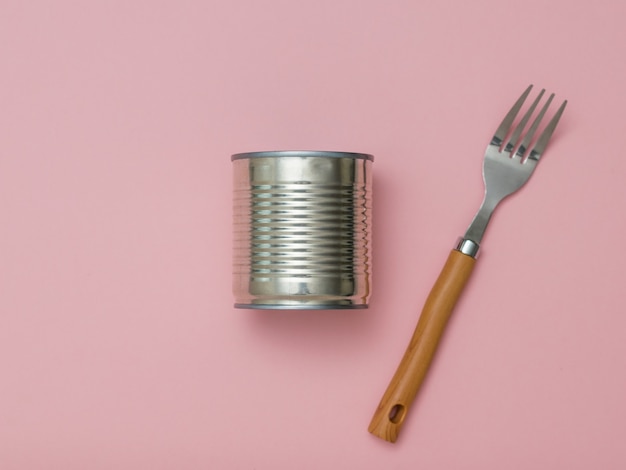 Gesloten blikje en vork op een roze achtergrond. universele container voor inblikken.