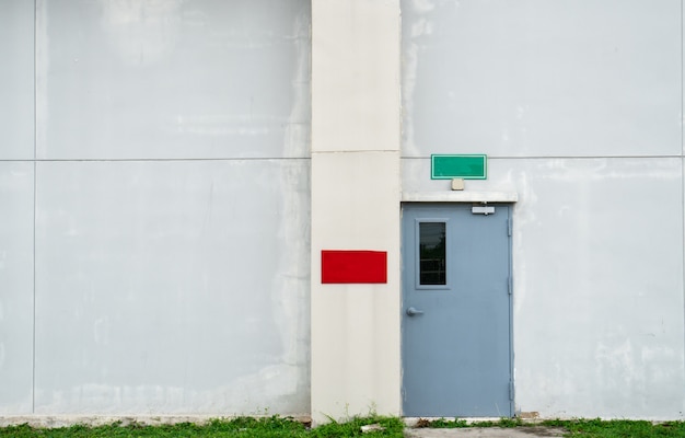 Gesloten grijze deur met groen en rood tekstvakje op witte concrete muur met exemplaarruimte