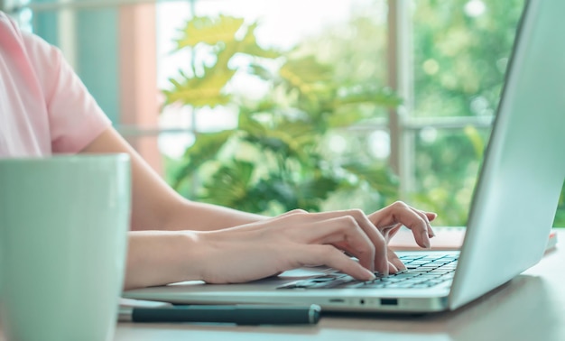 Foto gesloten opname van een vrouwenhand die op laptop thuis werkt met groene tuin op de achtergrond