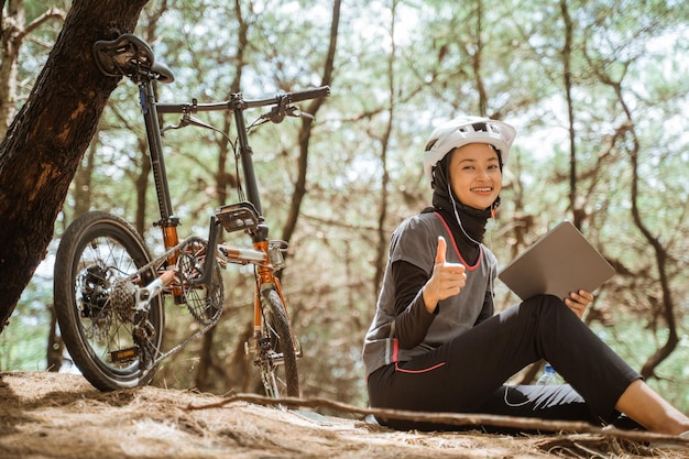 Gesluierd meisje dat oortelefoons draagt met duimen omhoog tijdens het fietsen