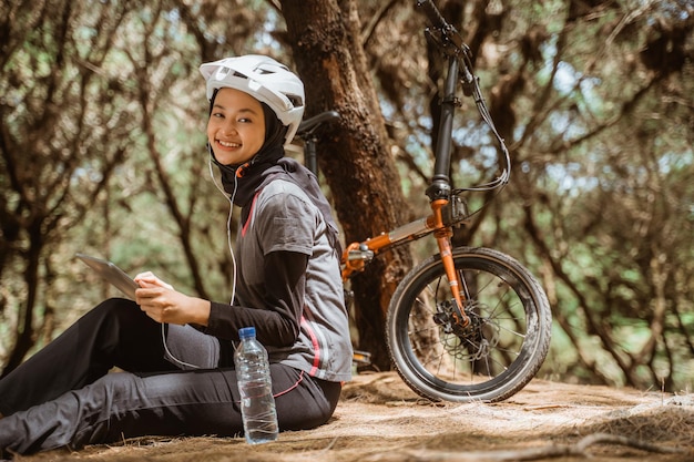 Gesluierd meisje zit te rusten fietsen met oortelefoons en met behulp van tablet