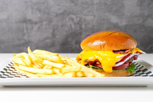 Foto gesmolten cheeseburger met frietjes op een witte tafel met een grijze achtergrond