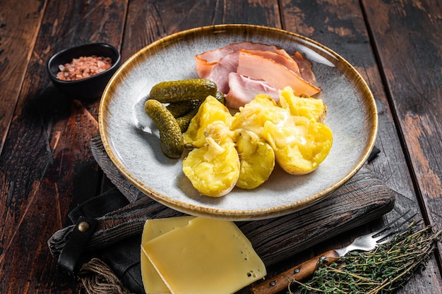 Gesmolten Raclette Zwitserse kaas met gekookte aardappel en ham Houten achtergrond Bovenaanzicht