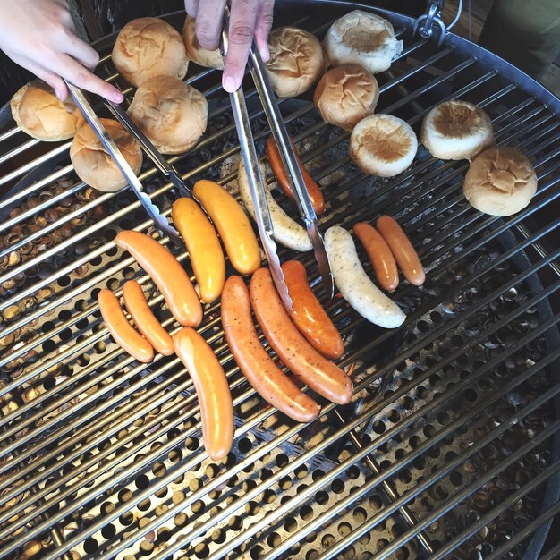 Foto gesneden afbeelding met de hand die worst op de grill bereidt