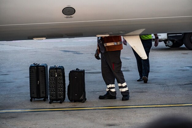 Foto gesneden afbeelding van een werknemer die passagiers bagage naar het vliegtuig brengt