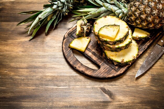 Gesneden ananas op een snijplank met een mes. Op een houten tafel.