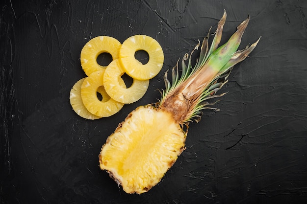 Gesneden ananas set, op zwarte donkere stenen tafel achtergrond, bovenaanzicht plat lag