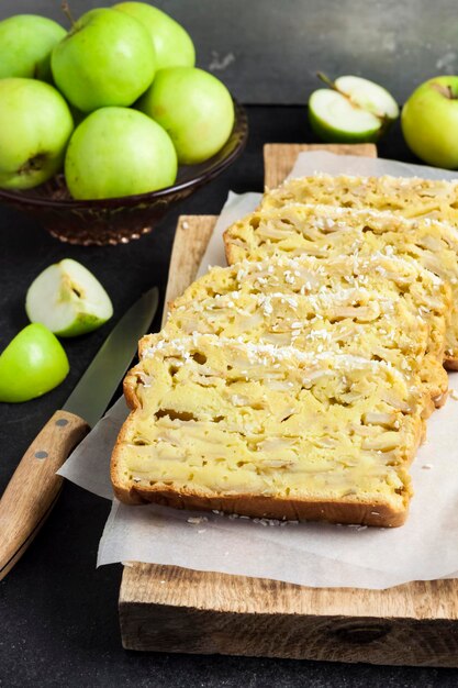 Gesneden appel en kokos oaf cake op houten snijplank op donkere achtergrond