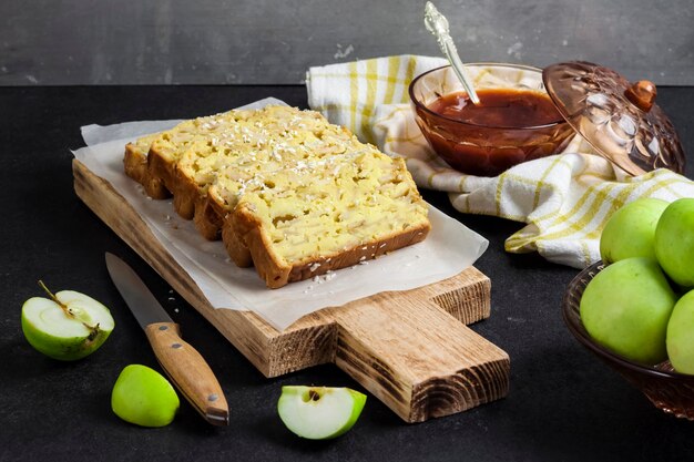 Gesneden appel en kokosnoot oaf cake op houten snijplank op donkere achtergrond