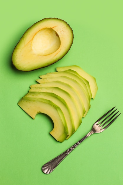 Gesneden avocado met een vork op een groene achtergrond