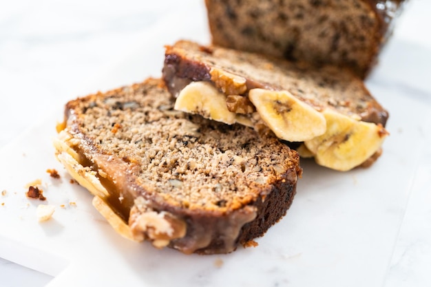 Gesneden bananennotenbrood besprenkeld met zelfgemaakte karamel op een marmeren snijplank.