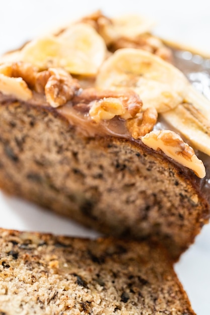 Gesneden bananennotenbrood besprenkeld met zelfgemaakte karamel op een marmeren snijplank.