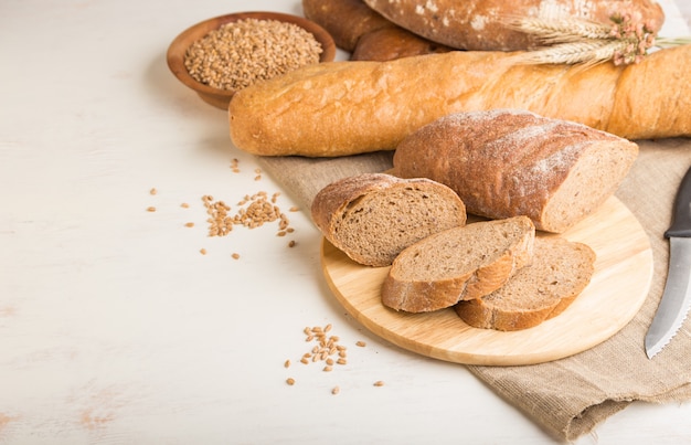 Gesneden brood met verschillende soorten vers gebakken brood op een witte houten muur. zijaanzicht, kopieer ruimte.