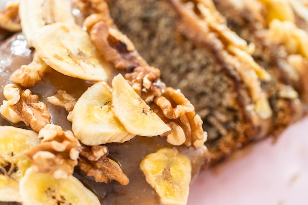 Gesneden brood van bananennotenbrood besprenkeld met zelfgemaakte karamel op een roze snijplank.