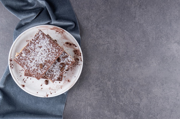 Gesneden chocoladetaart in witte plaat op stenen tafel.