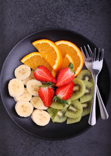 Gesneden fruit (aardbeien, kiwi, sinaasappel, banaan) op een zwarte plaat