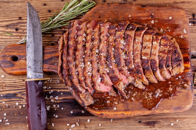 Gesneden gegrilde biefstuk met kruiden en mes op houten snijplank