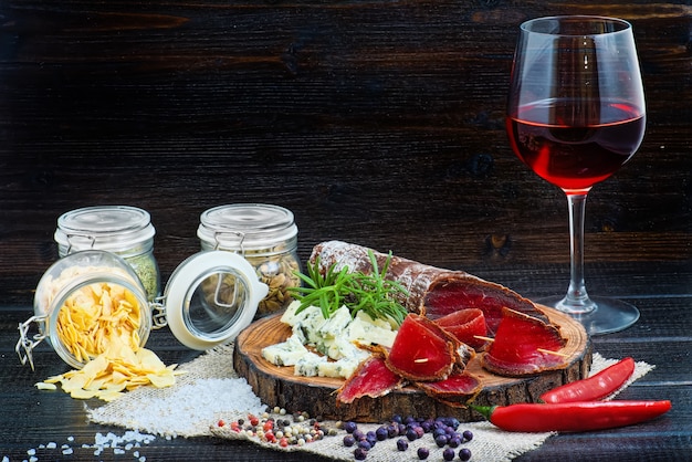 Foto gesneden genezen bresaola met kruiden en een glas rode wijn op donkere houten rustieke achtergrond.