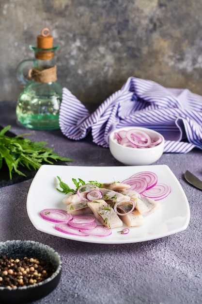 Gesneden gezouten haring met uien en rucola op een bord op tafel Eenvoudige snack Verticale weergave