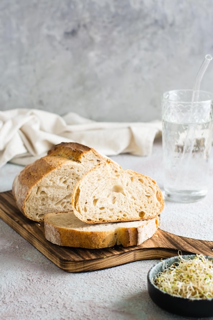 Gesneden graanbrood met zemelen op een snijplank, microgroenten en een glas water op tafel Biologische voeding Verticale weergave