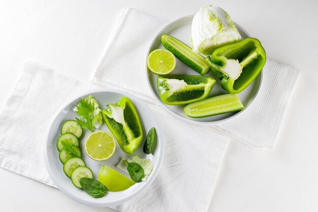 Gesneden groene groenten en fruit op platen. Groen dieetvoedsel op witte achtergrond. Gezond en vegetarisch eten. Bovenaanzicht