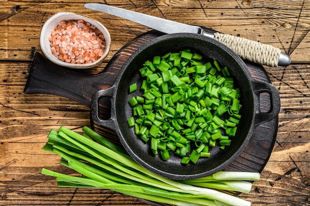 Gesneden Groene uien in een pan. houten achtergrond. Bovenaanzicht.