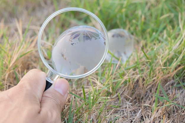 Foto gesneden hand van een man met een vergrootglas tegen een kristallen bol op grasland