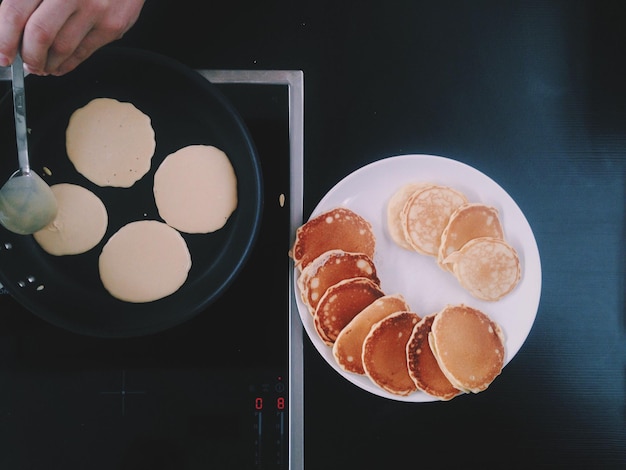 Gesneden hand van een persoon die pannenkoeken op de kachel kookt