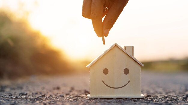 Gesneden hand van een persoon die tijdens de zonsondergang een munt in een modelhuis op het land zet
