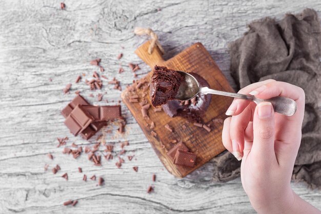 Gesneden hand van een vrouw die een chocoladekoek in een lepel boven de tafel houdt