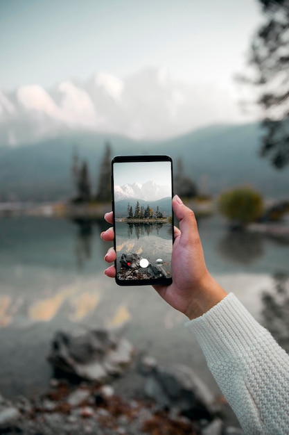 Gesneden hand van een vrouw die met een mobiele telefoon tegen het meer fotografeert
