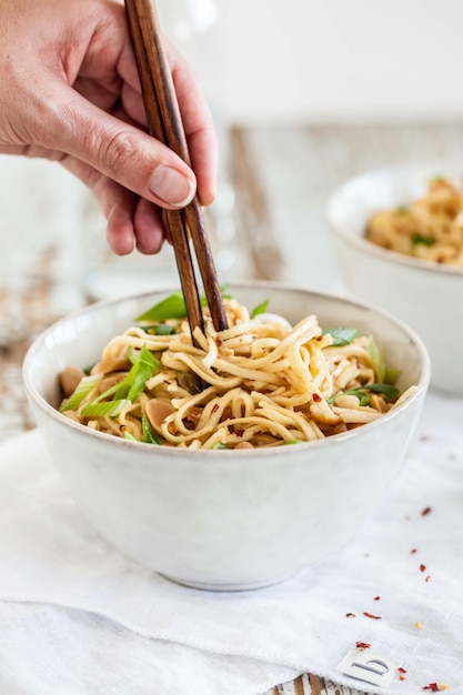 Gesneden hand van een vrouw die noedels eet met eetstokjes in een schaal op tafel
