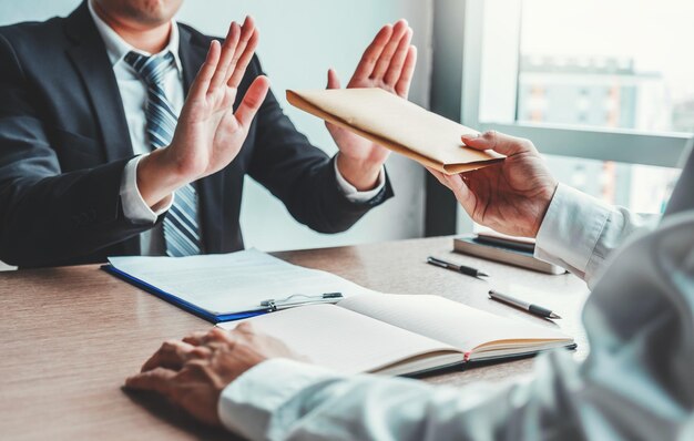 Gesneden hand van man die omkoping geeft terwijl zakenman weigert te accepteren op tafel