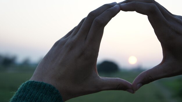 Foto gesneden handen die tegen de hemel gebaren tijdens zonsondergang