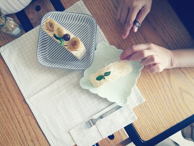 Foto gesneden handen van een vrouw die dessert aan tafel heeft.