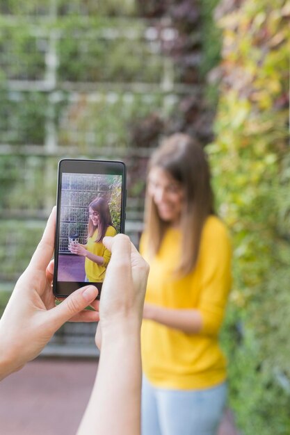 Foto gesneden handen van een vrouw die een vriend fotografeert met een mobiele telefoon tegen planten